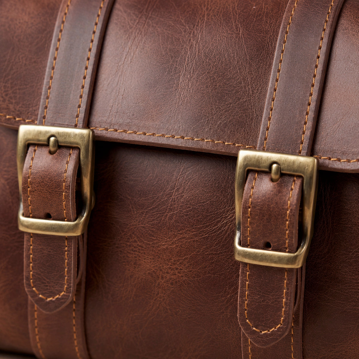 Close-up of Velora Ellis showing the twin brass-toned buckle closures, stitched leather straps, flap construction, and leather grain.